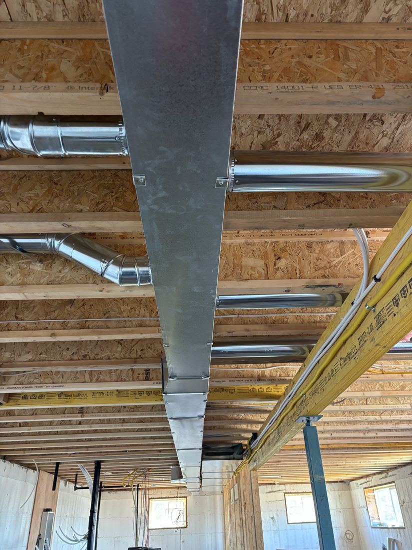 Galvanized sheet metal ductwork and round duct runs between floor joists in an unfinished basement