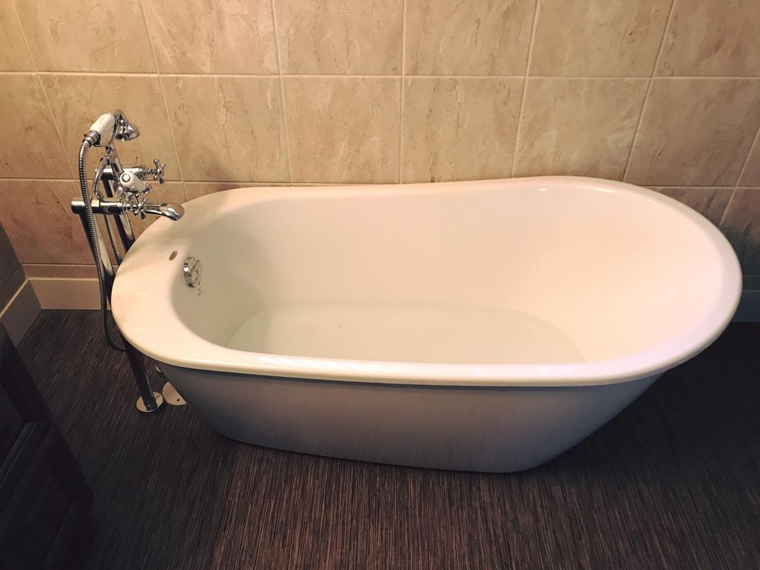 White freestanding bathtub with a floor-mounted tub filler in a tiled bathroom