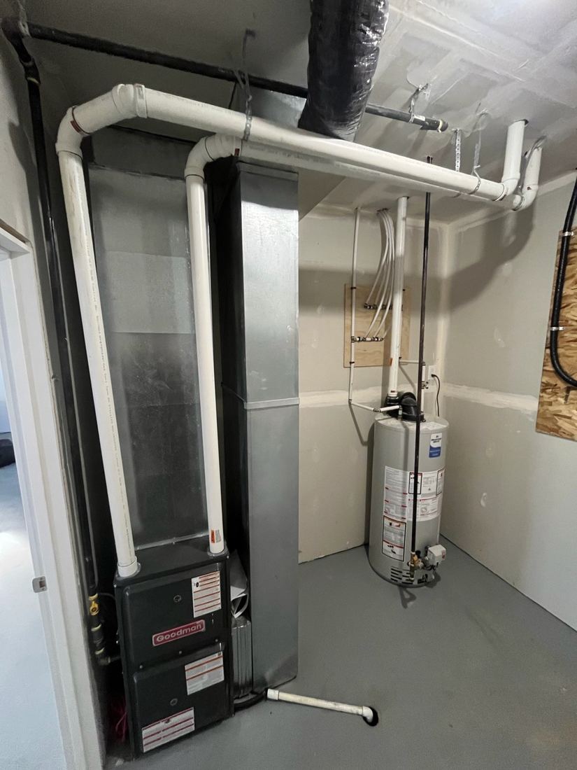 Gas furnace with white venting pipes and ductwork, and a gas water heater, in a finished utility room