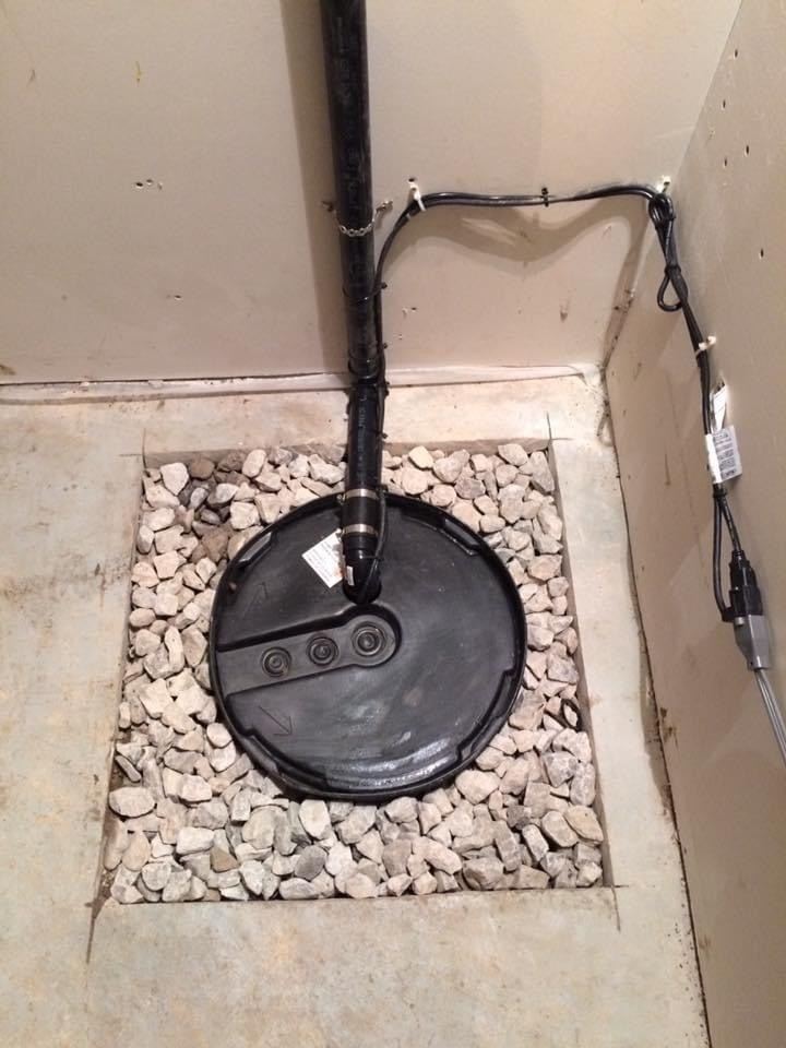 Sump pit with a black pump lid set in a bed of gravel in a basement floor