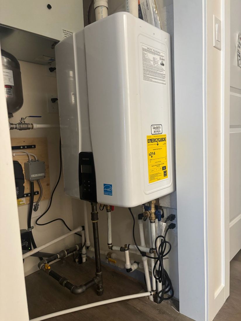 Wall-mounted tankless water heater with white venting and water and gas piping below