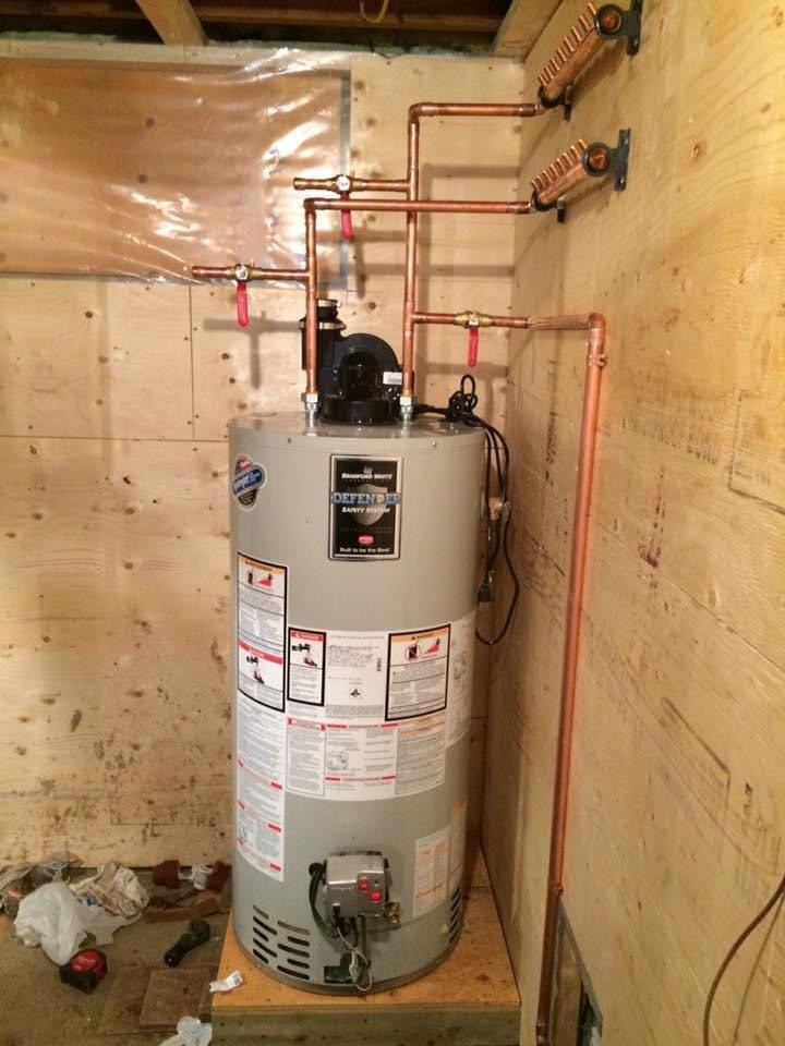 Gas water heater connected to copper piping with shut-off valves in a plywood-lined room